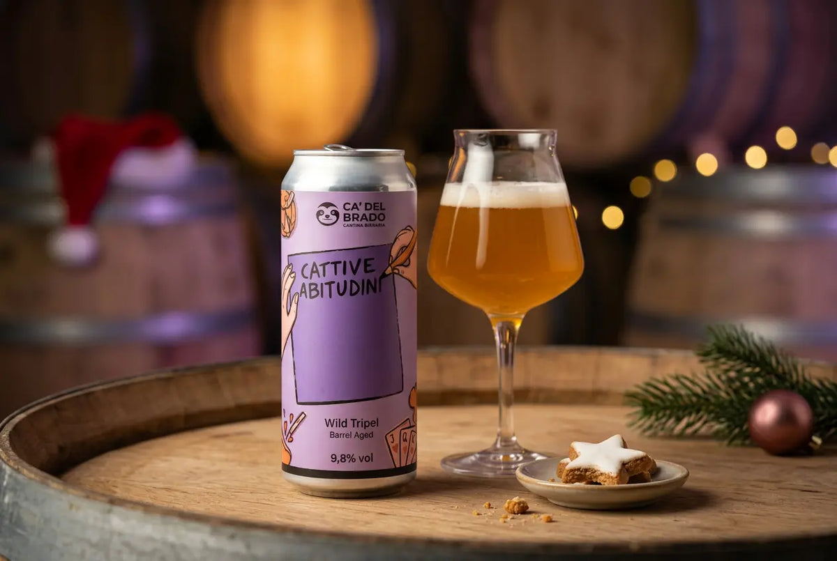 Cattive Abitudini beer can and glass with golden wild tripel, on a wooden barrel background.